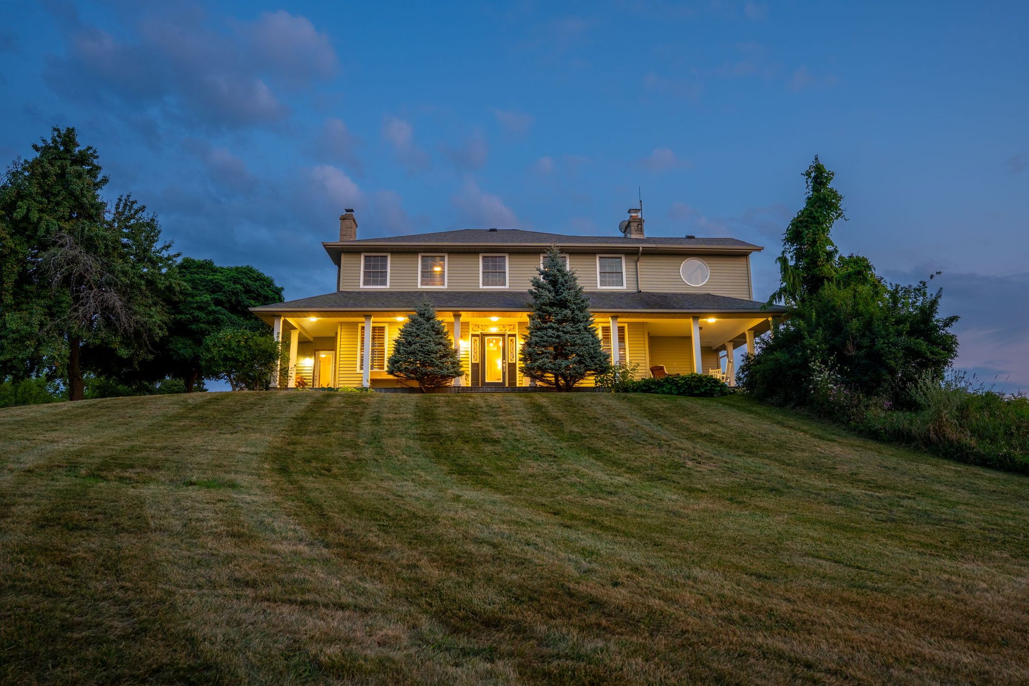 The main residence on its rise with every window lit at dusk